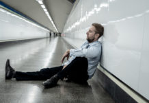 Social Determinants of Health and the Continued Individualization of Suffering man sits on floor against wall of tunnel