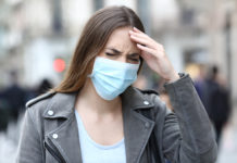 Is COVID-19 Making Everybody Crazy? woman holding her head annoyed wearing medical mask