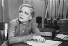 ADHD as Cargo Cult Science Black and white photograph depicting a seated woman looking up thoughtfully from a pile of papers on a desk