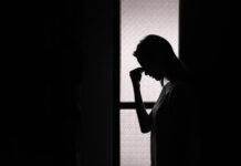 Mental Health Care Must Support Consent and Basic Human Rights Photo of a person sihouetted against a window holding their face with their hand, looking sad or in pain