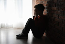 Why Is Child Sexual Abuse So Common in Institutions? Photo of a boy sitting against a brick wall with his hands covering his face
