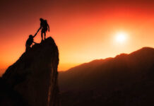Ending Coercive “Help”: A Review of “Reimagining Crisis Support” Photo of two silhouetted people on top of a rock at sunset. One is helping the other.