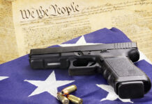 US Gun Culture Connected to Elevated Youth Suicide Rates A 45 caliber handgun and ammunition resting on a folded flag against the United States constitution.
