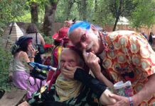 July is Both Disability Pride Month and Mad Pride Month: Happy Bastille Day! Blog author, David Oaks, in wheelchair with Patch Adams, with blue hair and glasses. Both are picking their noses at the Oregon Country Fair, with trees in the background. Oaks says, "Searching for meaning."