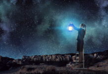 Grief, Intense Feelings, and Pathologization: Can We Conceive a Different Approach? A woman in a suit with a skirt holds a lantern while standing on a desert landscape below a night sky full of stars