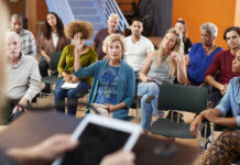 20 Concrete Steps to Achieving System Change Seated among others at a town hall meeting, an older adult white woman raises her hand