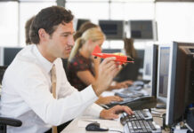 Meaningless Distractibility, or Meaningful Mind-Wandering? Photo of a man in a white button-down and tie, sitting at a desk in an office, with one hand on a computer keyboard and the other holding a red toy airplane