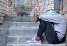 The “S” Word: How the Culture of Fear Has Failed Youth in Crises A black teen in a hooded sweatshirt sits on the stairs, hiding their face, looking depressed.