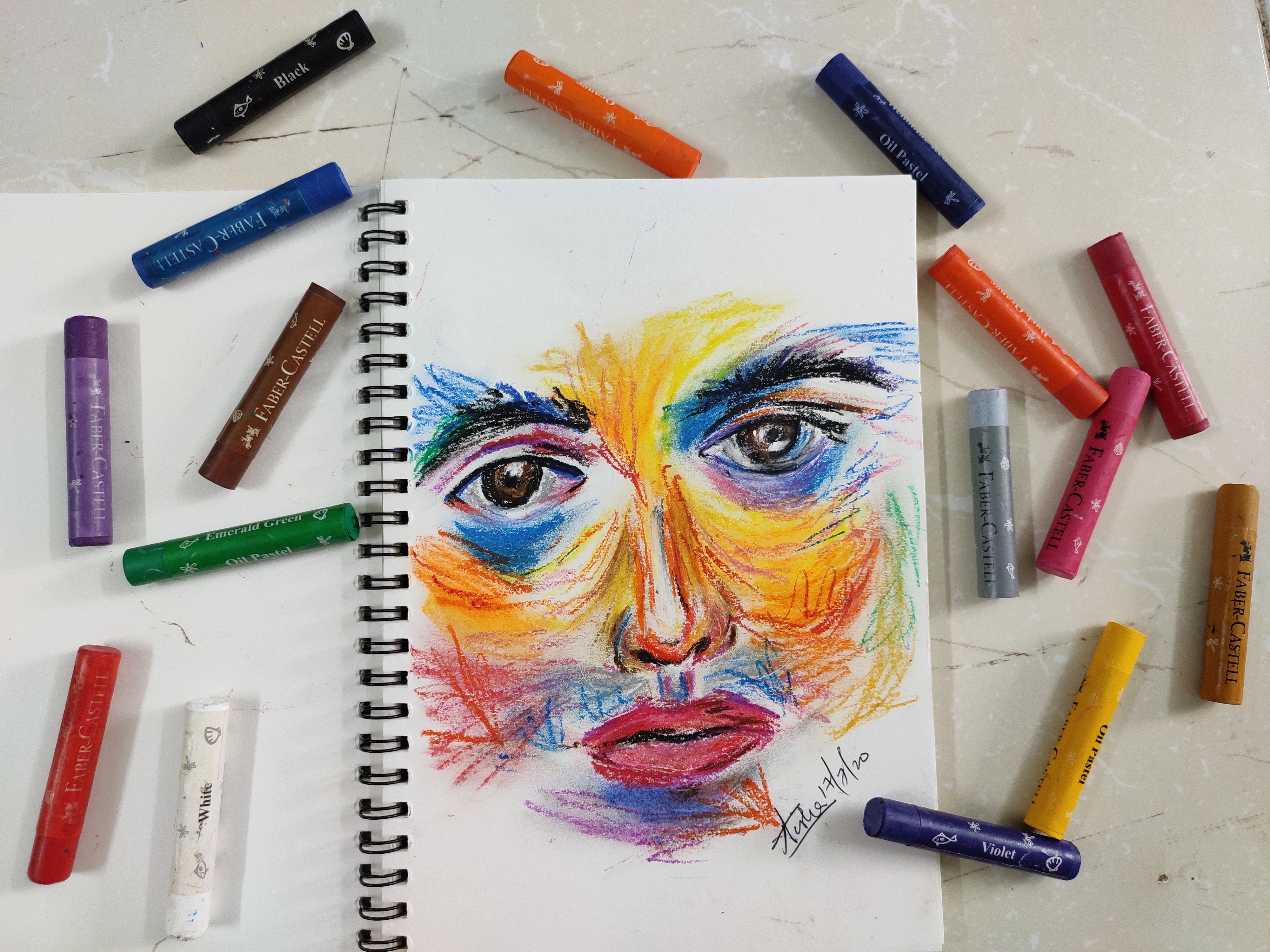 colorful face on paper, surrounded by oil pastels