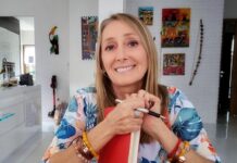 Threatened for Telling the Truth: Polish Journalist Speaks Out Beata Pawlikowska, a blonde White woman, smiles while holding a manuscript and a pen, sitting at a table in a home.