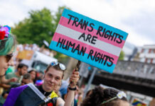 LGBTQIA+ Peer Respites: The Personal Is Political A person outside holding a sign with the trans flag that reads "TRANS RIGHTS ARE HUMAN RIGHTS"
