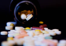 The Systemic Harms of Psychiatry A bottle of spilled pills on black background.