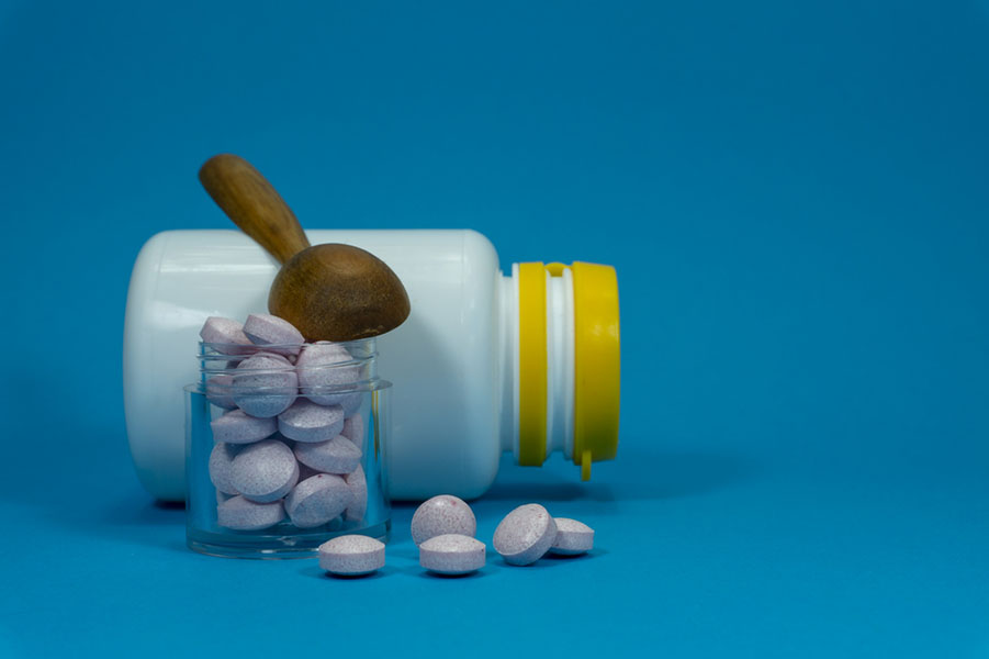 Pills spilling out of a white bottle on a blue background