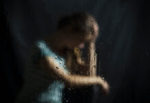 The War on Suicide Is Making Things Worse A girl looks sad, blurry through a rainy pane of glass, dark