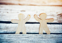 Reimagining Crisis Support: A Conversation with Tina Minkowitz Wooden little men holding hands on natural sunlight background. Symbol of friendship, love and teamwork