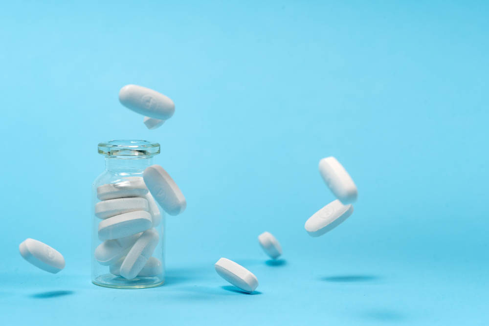 White pills bounce out of clear bottle on blue background