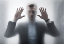 Are “Trauma/Addiction Experts” and Psychiatrists Misleading Us? Man with hands against glass, out of focus, looking distressed
