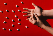 Much of U.S. Healthcare Is Broken: How to Fix It (Chapter 2, Part 6) Photo of an open hand on a deep red background with scattered white pills