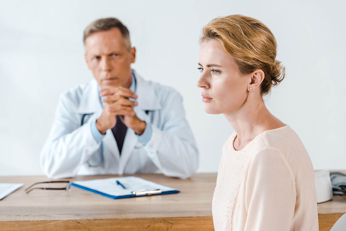 A male doctor looks slightly angry at a woman who looks sad in profile