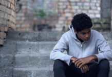 Trauma and Resources Within Social Context A young man sitting on steps outside looking sad