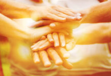 The Integration of Peer Support Principles in Community Mental Health Policy and Practice: Toward Epistemic Humility Photo of hands stacking on top of each other in very yellow light