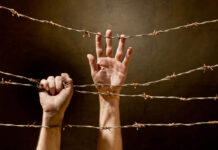 The “Madness” of Inpatient Psychiatry hand behind barbed wire with dark background