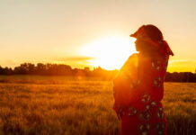 From a Paranoid Schizophrenia Diagnosis to a Peer Researcher in Nigeria African woman in traditional clothes standing, looking, hand to eyes, in field of barley or wheat crops at sunset or sunrise