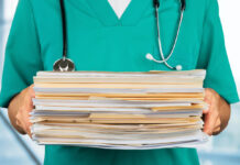 Is Public Psychiatry Responding to the Mental Health Crisis or Just “Treating the Chart?” Closeup shot of a figure in blue/green scrubs holding a pile of paperwork and folders