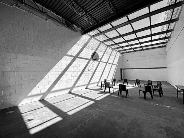 Black and white photo of a large room with chairs in a circle, striking light and shadow