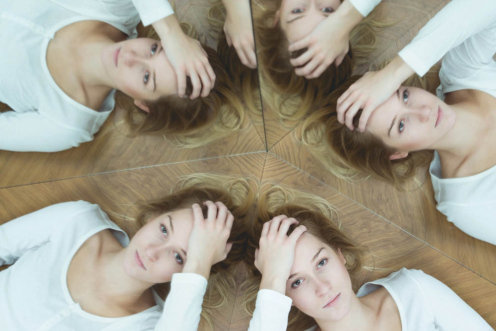 Photo of a white woman reflected in five mirrors holding her head