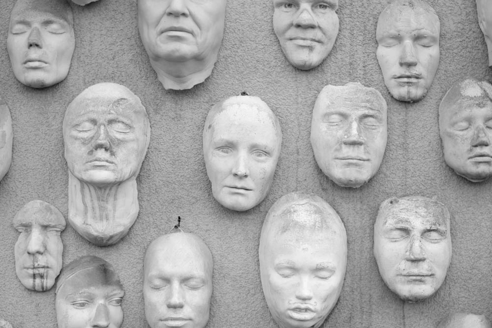 Black and white photo of a wall with faces on it like masks
