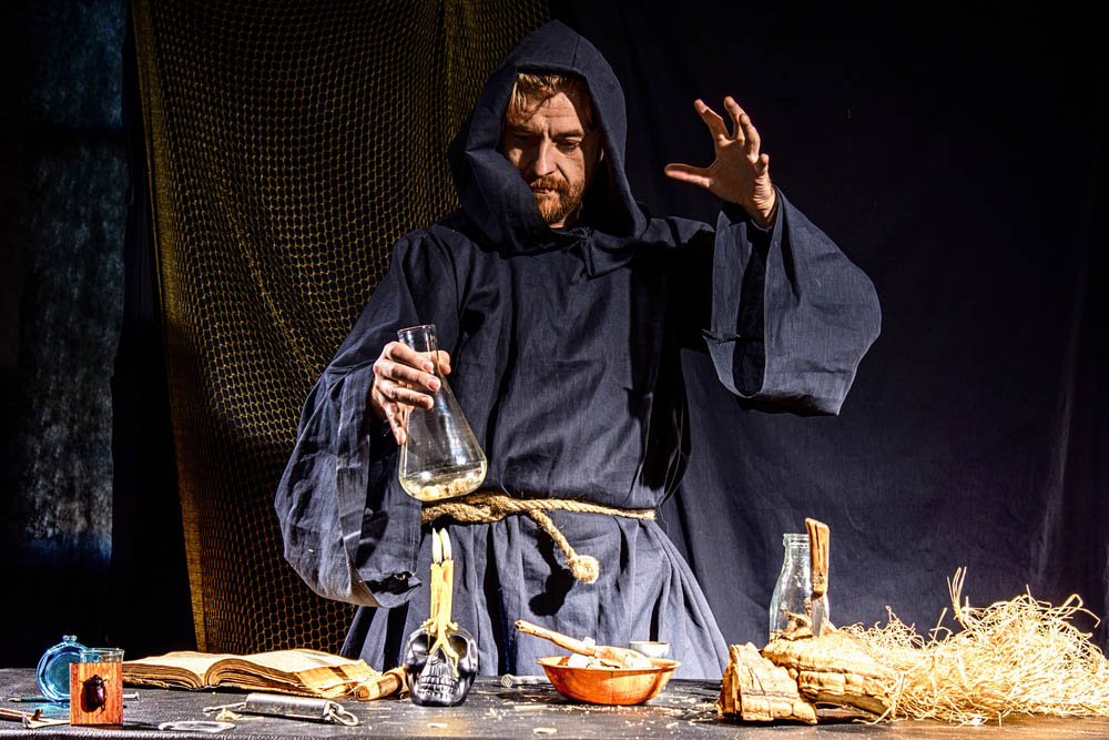 Photo of a man dressed in a plain robe doing alchemy with a glass jar over a candle