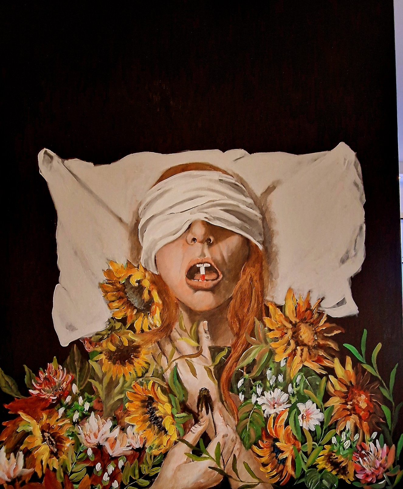 A painting of a woman covered in flowers, her head rests on a pillow, a white cloth is wound around her head covering her eyes and her mouth is open with a medicine capsule held between her teeth.