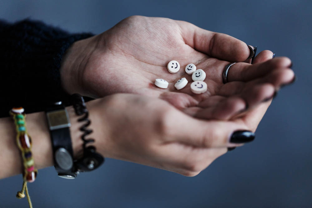 Photo of cupped hands holding little pills with smiley faces on them