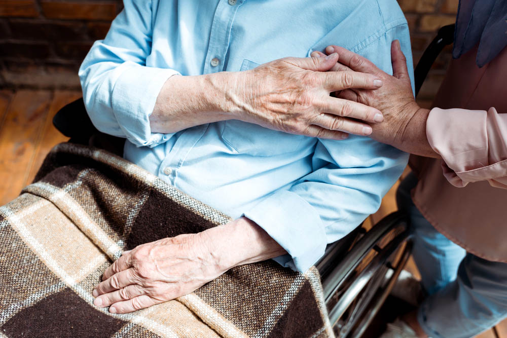 Older adult sitting with a blanket in lap, holding the hand of someone else out of frame