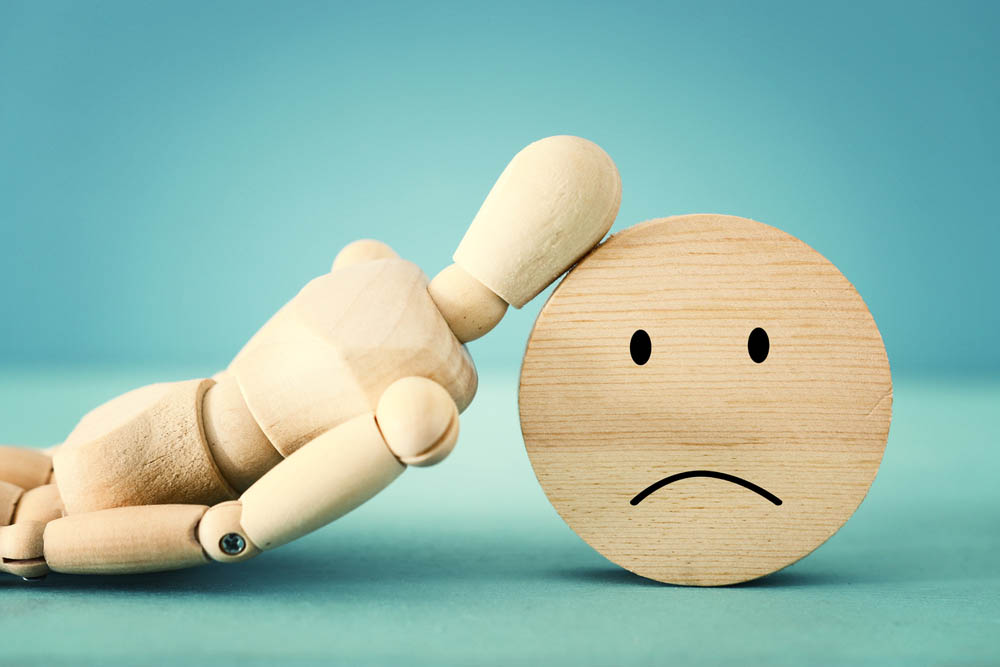 art mannequin leaning on a sad face wood block