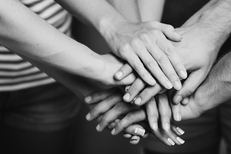 Black and white photo of many hands laid on top of each other