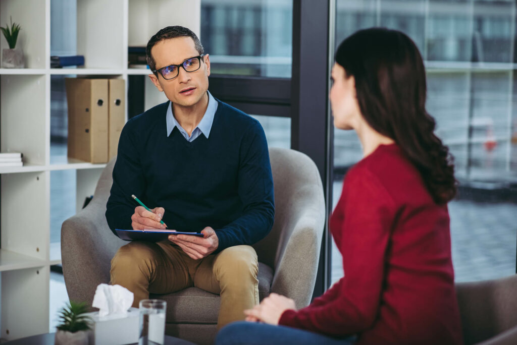 male psychologist listening to woman and making notes in document on clipboard