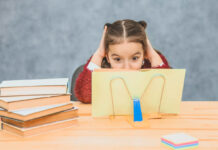 New Guidelines on How to Accurately Convey ADHD Information A sweet girl schoolgirl on a gray background. Works homework by reading a book in a yellow cover.
