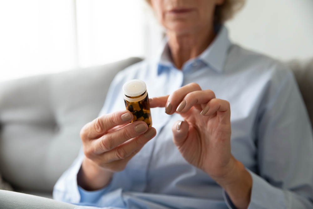 Seated older woman (face out of frame) holding pill bottle to read the label