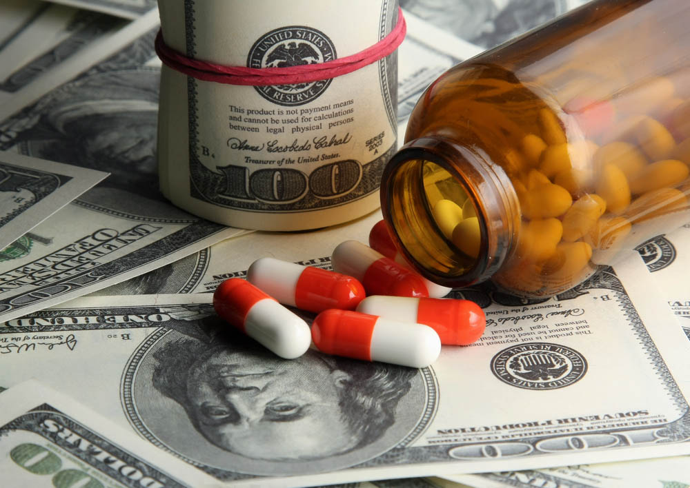 A bottle of pills tipped over, spilling red and white pills onto a pile of hundred dollar bills