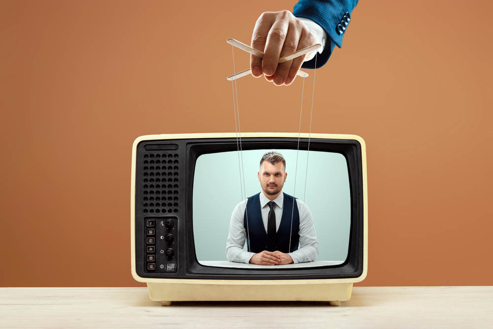 The puppeteer's male hand manipulates the news announcer in the TV