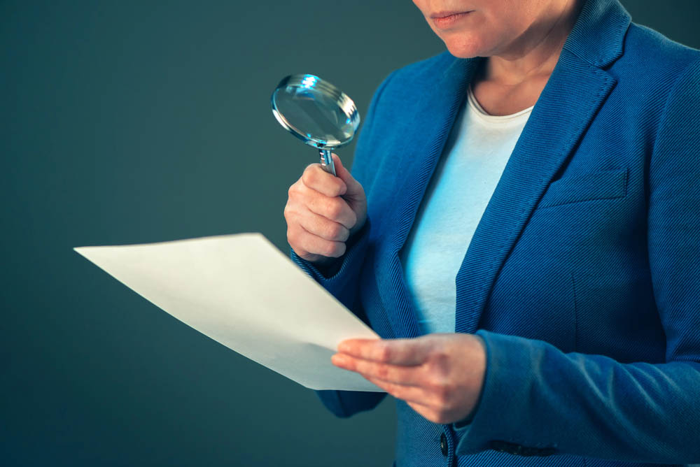 Professional woman looking at documents with magnifying glass