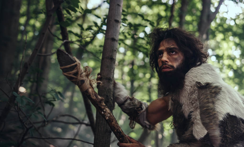 Portrait of Primeval Caveman Wearing Animal Skin and Fur Hunting with a Stone Tipped Spear in the Prehistoric Forest. Prehistoric Neanderthal Hunter Ready to Throw Spear in the Jungle