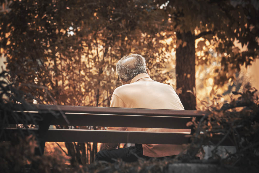 senior man sitting alone. Lonely gray haired man on a bench in fall season