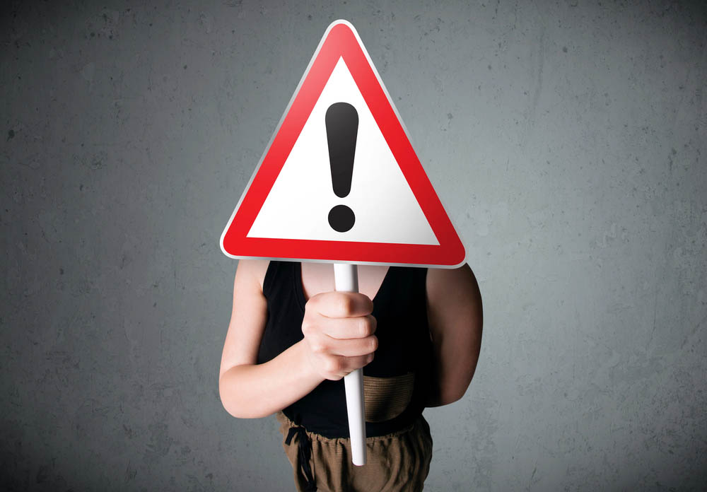 Stock image of a person holding a warning sign in front of their face.