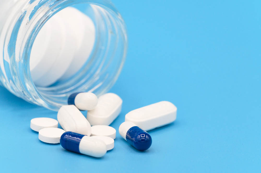 Close up of Pills spilling out of pill bottle on blue background. with copy space. Medicine concept .