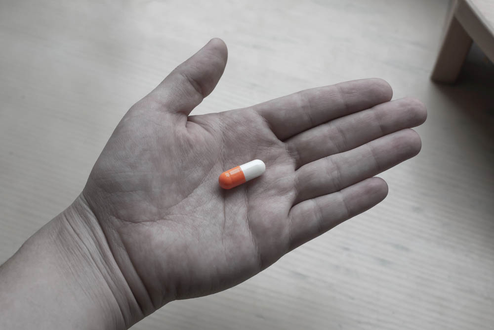 Black and white photo of a hand holding a colorized pill
