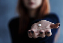Behind the Smiles: Mental Health in South Korea’s High-Pressure Society Close-up of pill with smiley face on it. Woman's hand holding it toward the viewer