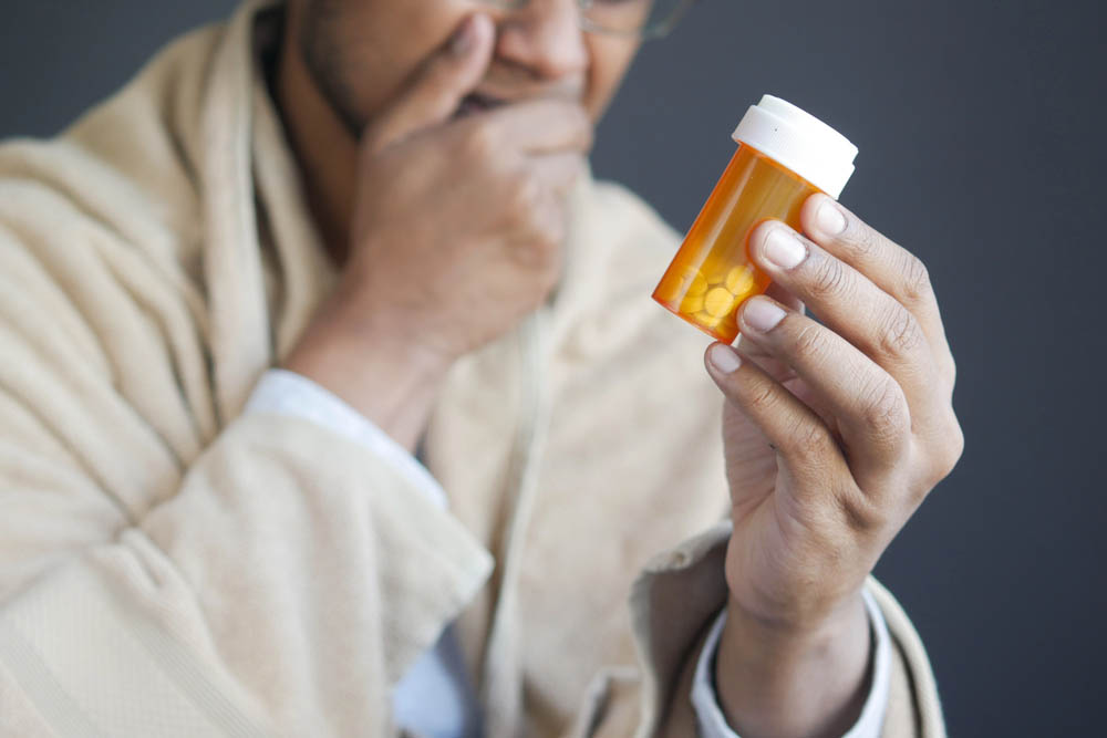 A person, out of focus, holding a pill bottle in focus